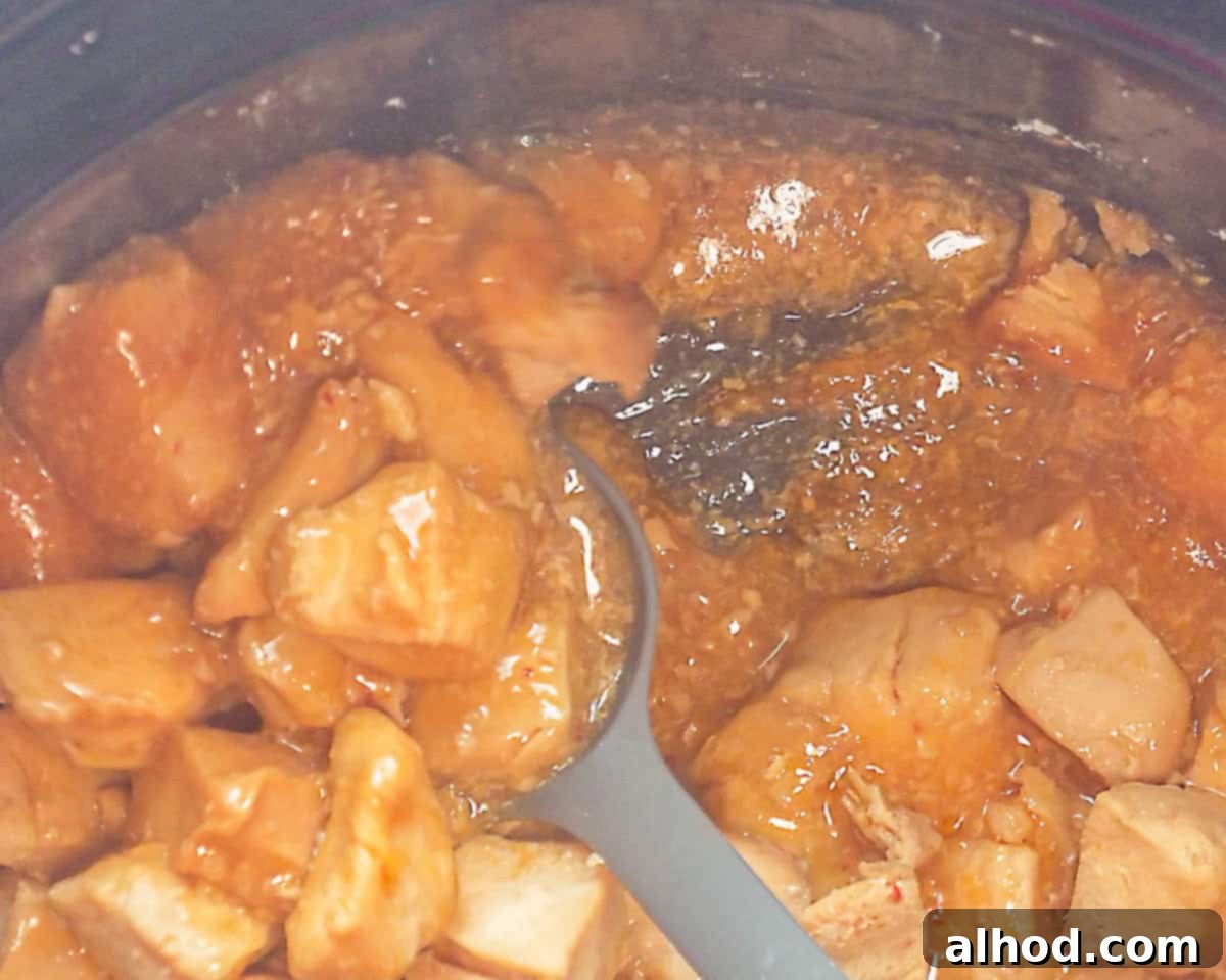 Easy Honey Garlic Slow Cooker Chicken 7 A slow cooker with cooked honey garlic chicken, to which a cornflour slurry has been added and is now being mixed