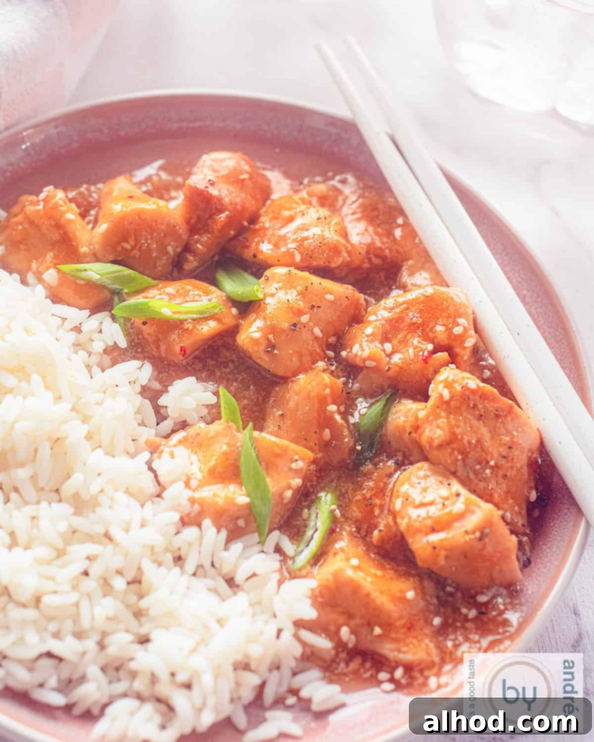 Easy Honey Garlic Slow Cooker Chicken 8 A height shot of a pink bowl filled with garlic honey marinated chicken from the slow cooker and rice.