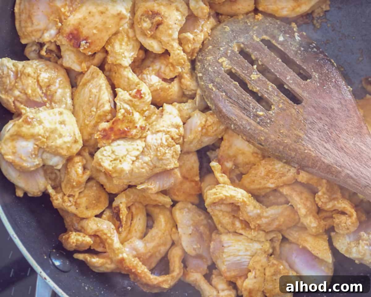 Whip Up Easy Chicken Jalfrezi: Dinner in Minutes 5 A high-angle shot of a wok on a stove, with seasoned chicken cubes sizzling and browning in hot oil, indicating the frying process.