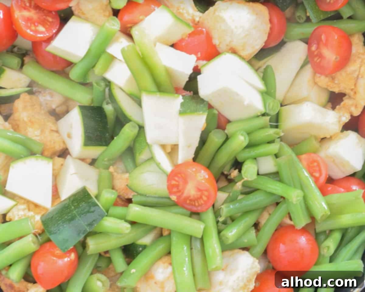 Whip Up Easy Chicken Jalfrezi: Dinner in Minutes 6 A colorful mixture of fried chicken and fresh, chopped vegetables including onions, zucchini, green beans, and cherry tomatoes, stir-frying in a wok.