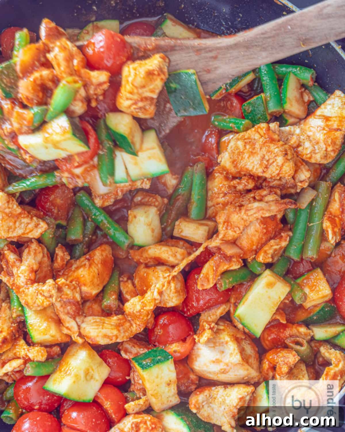 Whip Up Easy Chicken Jalfrezi: Dinner in Minutes 8 A top-down view of a large pan filled with freshly cooked Chicken Jalfrezi, showing the succulent chicken pieces and colorful vegetables swimming in a rich, vibrant sauce. A wooden spoon is stirring the curry, emphasizing its freshness and home-cooked appeal.