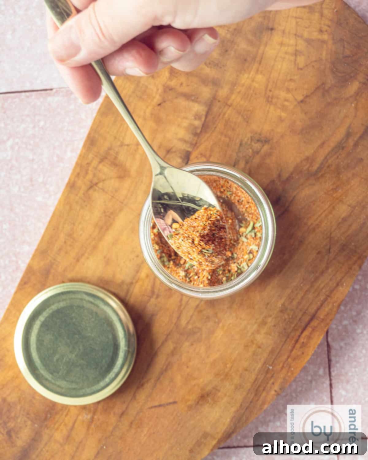 Homemade Taco Seasoning 2 An aerial photo of a wooden board with a glass jar of taco seasoning. A golden spoon scoops out a pile of seasoning.