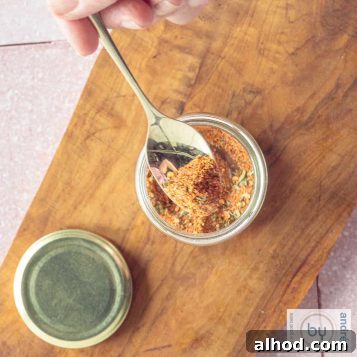 Homemade Taco Seasoning 4 A square photo from above, a glass jar with Mexican spices. A golden spoon scoops out a bite.