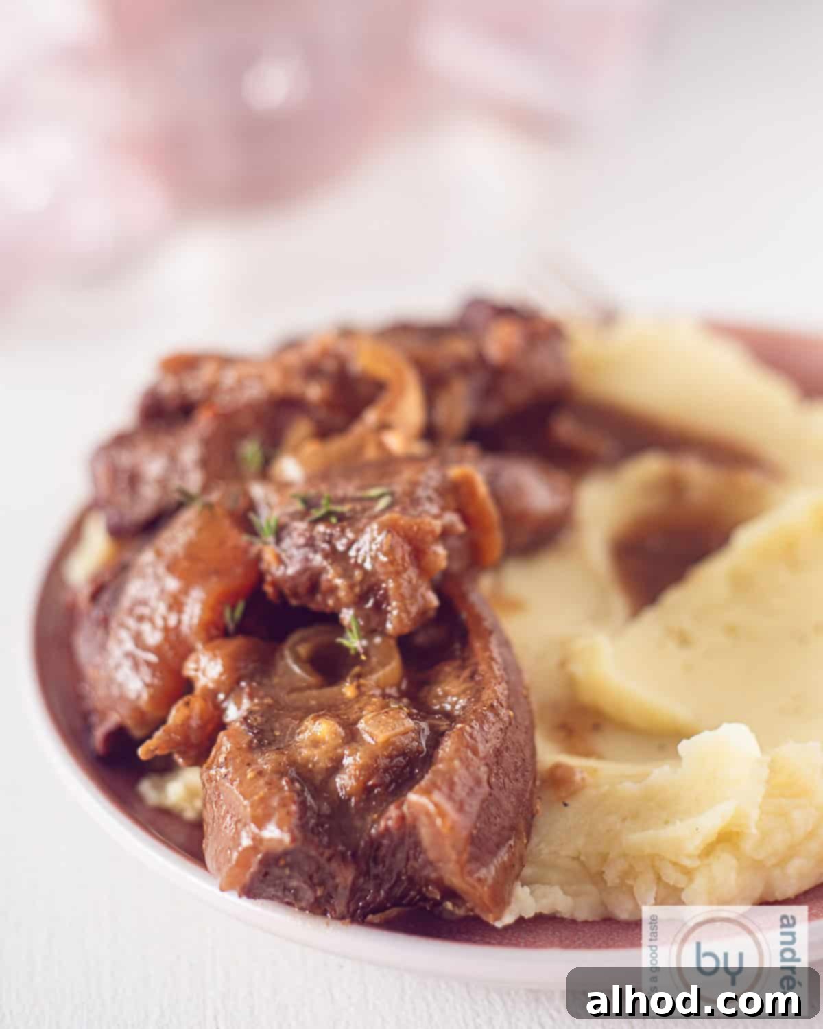 Melt-in-Your-Mouth Slow Cooker Dutch Sukadelapjes 2 A height photo of part of a pink plate with mashed potatoes, gravy and beef steaks.