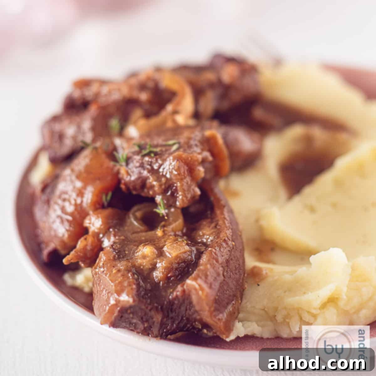 Melt-in-Your-Mouth Slow Cooker Dutch Sukadelapjes 9 A square photo with a pink plate with mashed potatoes, beef steaks in a rich gravy.