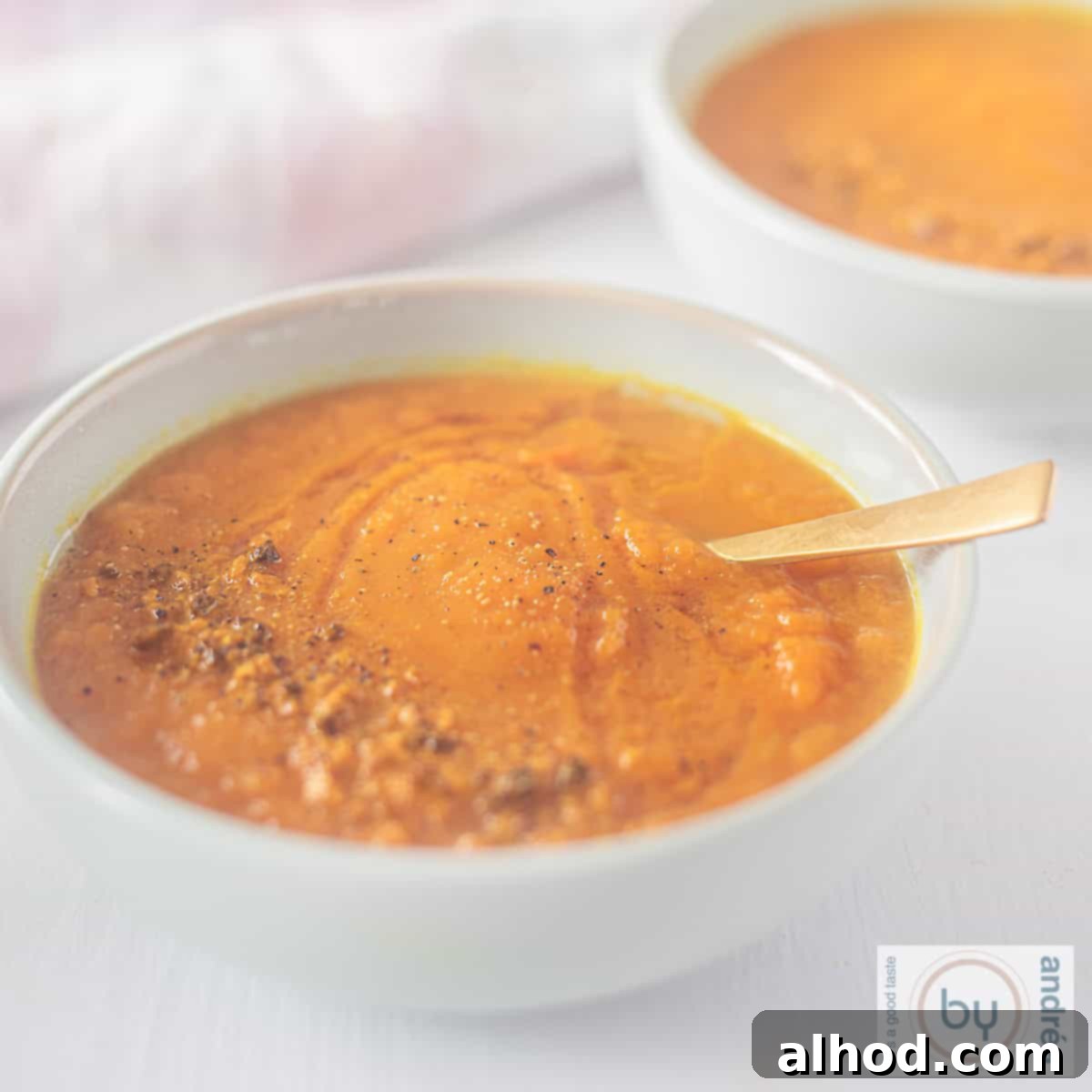 7 Incredible Asian Soups You Need to Taste 3 A square photo of a blue bowl filled with carrot curry soup. A golden spoon lies in the soup.