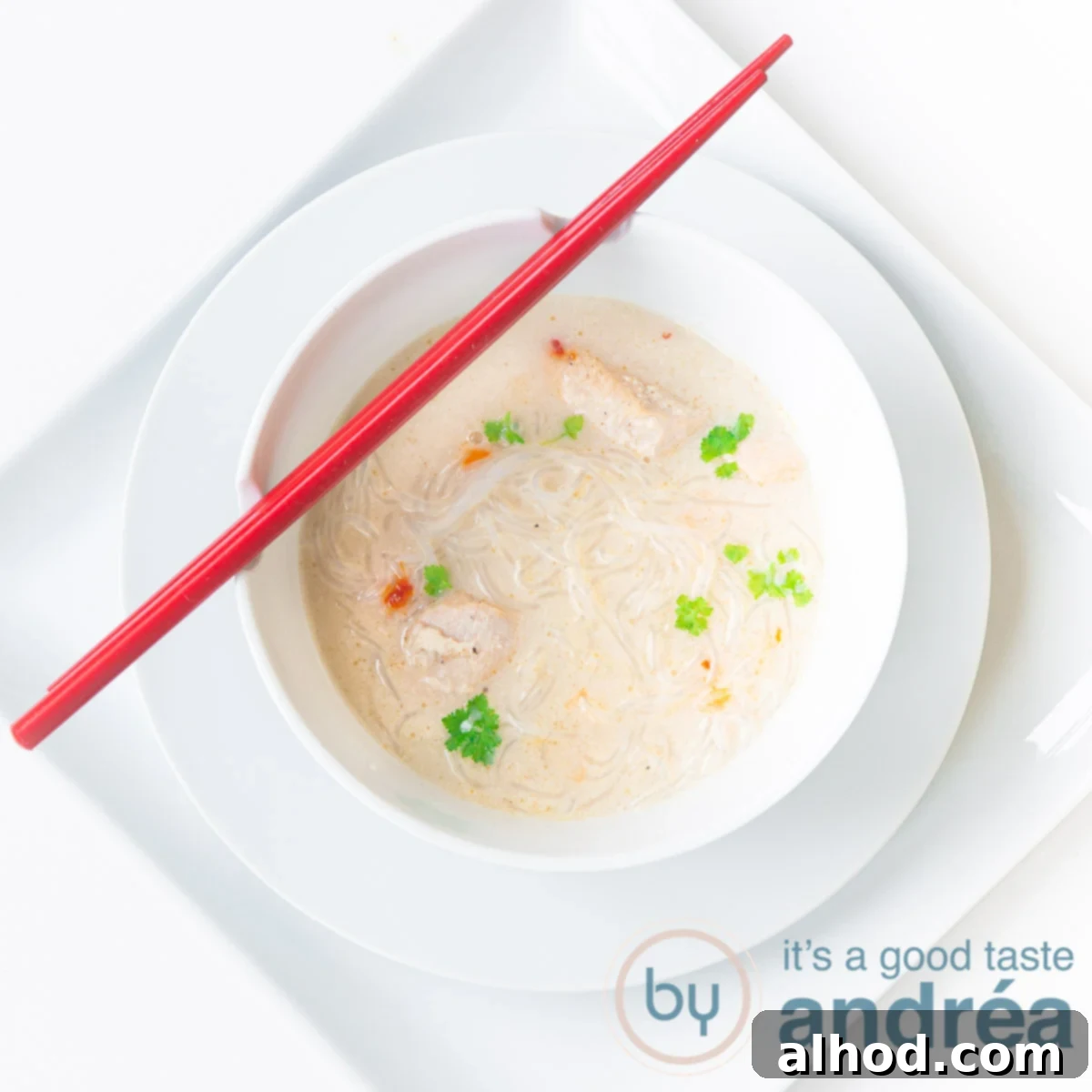 7 Incredible Asian Soups You Need to Taste 4 A square photo with a white background, a square plate, a round plate and a white soup bowl filled with creamy chicken soup. Two red chopsticks lie on it.
