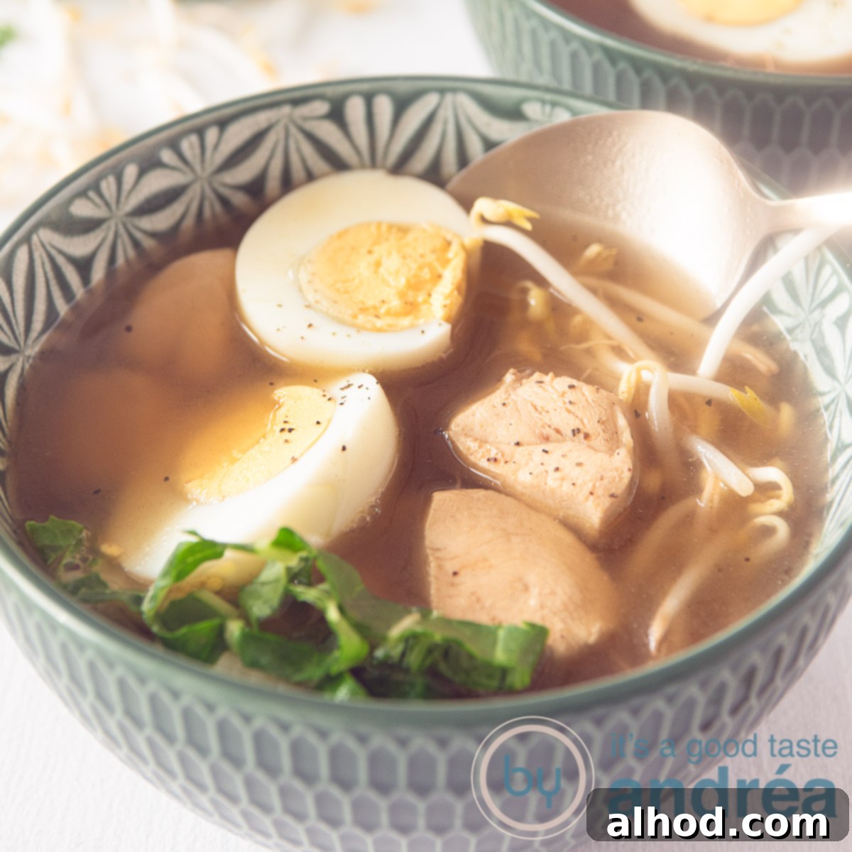 7 Incredible Asian Soups You Need to Taste 8 A square photo of a green bowl filled with Japanese noodle soup with chicken, bok choy, bean sprouts and eggs. A golden spoon takes a bite.