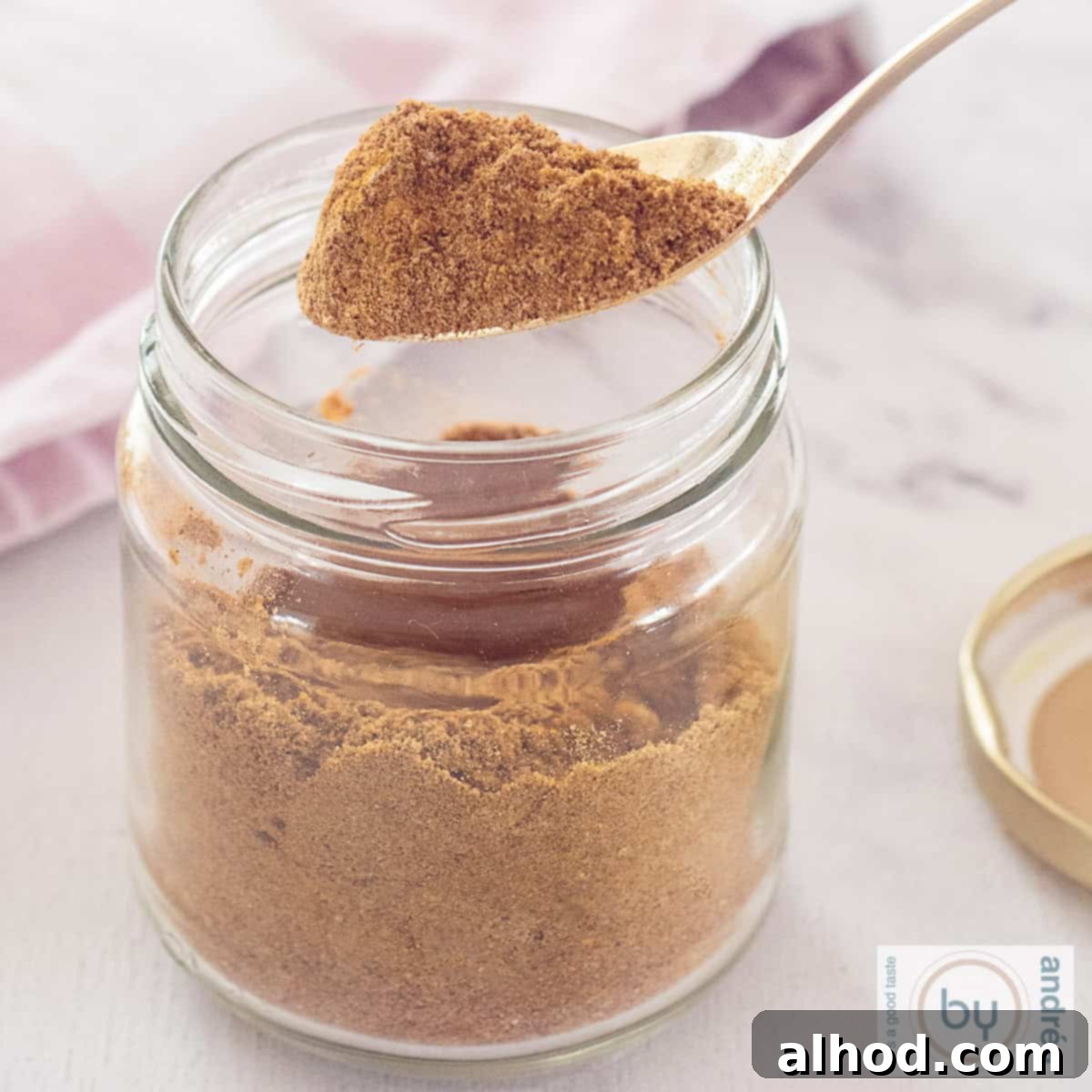 Authentic Homemade Madras Curry Blend 5 A square photo featuring a glass jar filled with a rich, reddish-brown Curry Madras spice mix. A golden scoop has been used to remove a small portion of the aromatic blend.