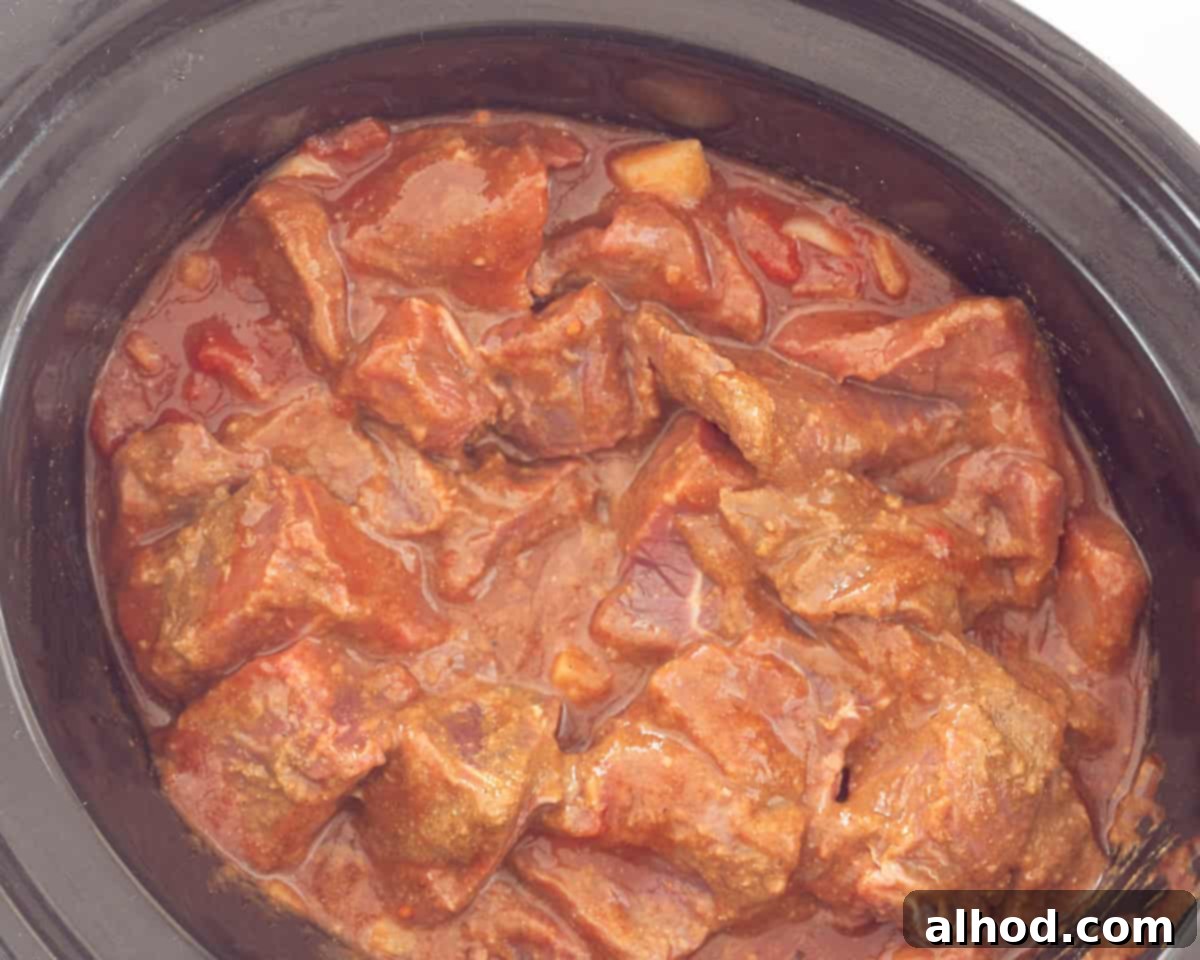 Tender Slow Cooker Beef Madras Curry 8 A slow cooker, its interior generously filled with a simmering, rich beef curry madras sauce, radiating warmth and aromatic spices.