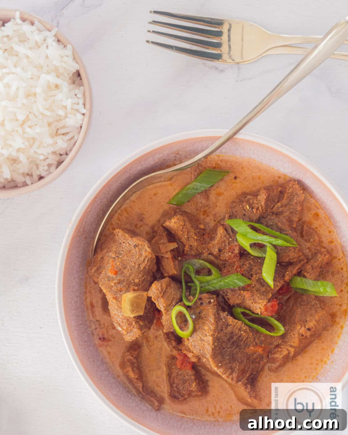 Tender Slow Cooker Beef Madras Curry 9 A high-angle shot showcasing a pink bowl filled with tender slow cooker beef madras curry, alongside a separate bowl of fluffy white rice, creating a comforting and complete meal.