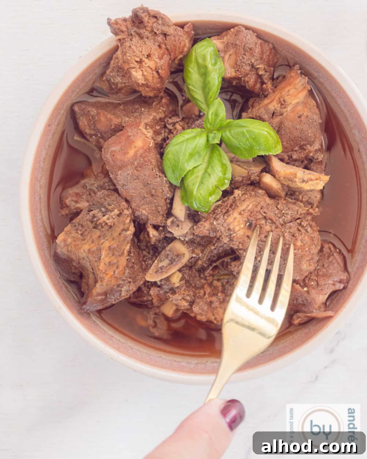 Peposo Tuscan Red Wine Beef Stew 2 A photo from above with a bowl filled with peposo, Italian stew in sauce. A fork pokes the tender meat