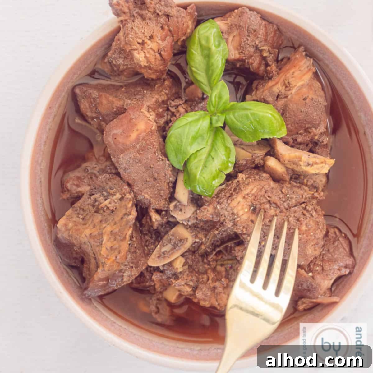 Peposo Tuscan Red Wine Beef Stew 9 A square photo of a pink bowl of peposo stew. A fork pokes the tender meat