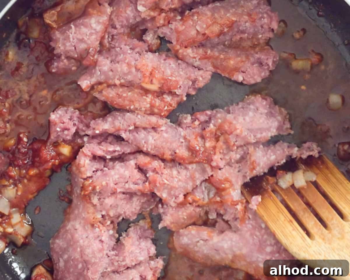 An onion, garlic and tomato paste are fried in a frying pan and ground beef is added and fried until crumbly.