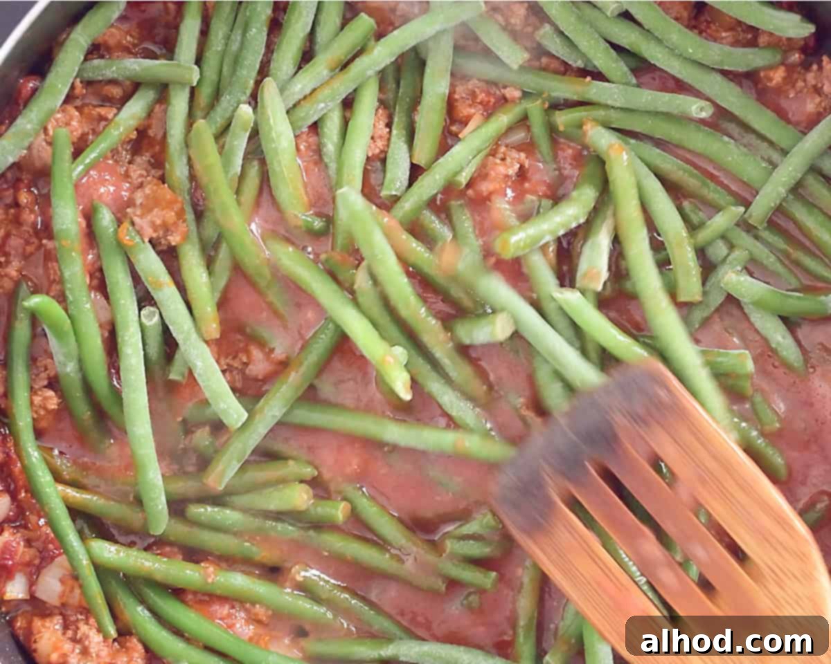 A casserole pan filled with minced meat in a tomato sauce and green beans on the stove.