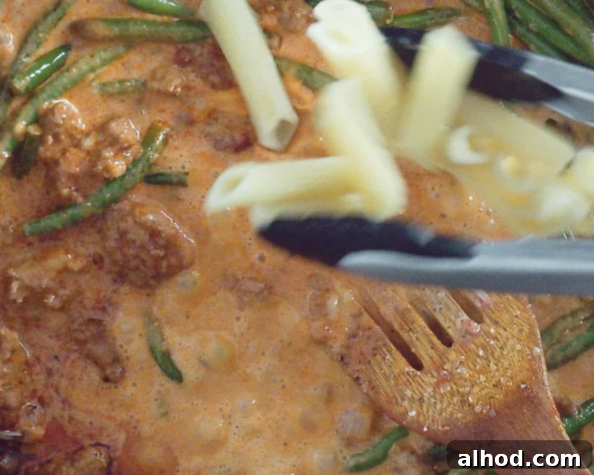 Penne is added to the rich tomato sauce.