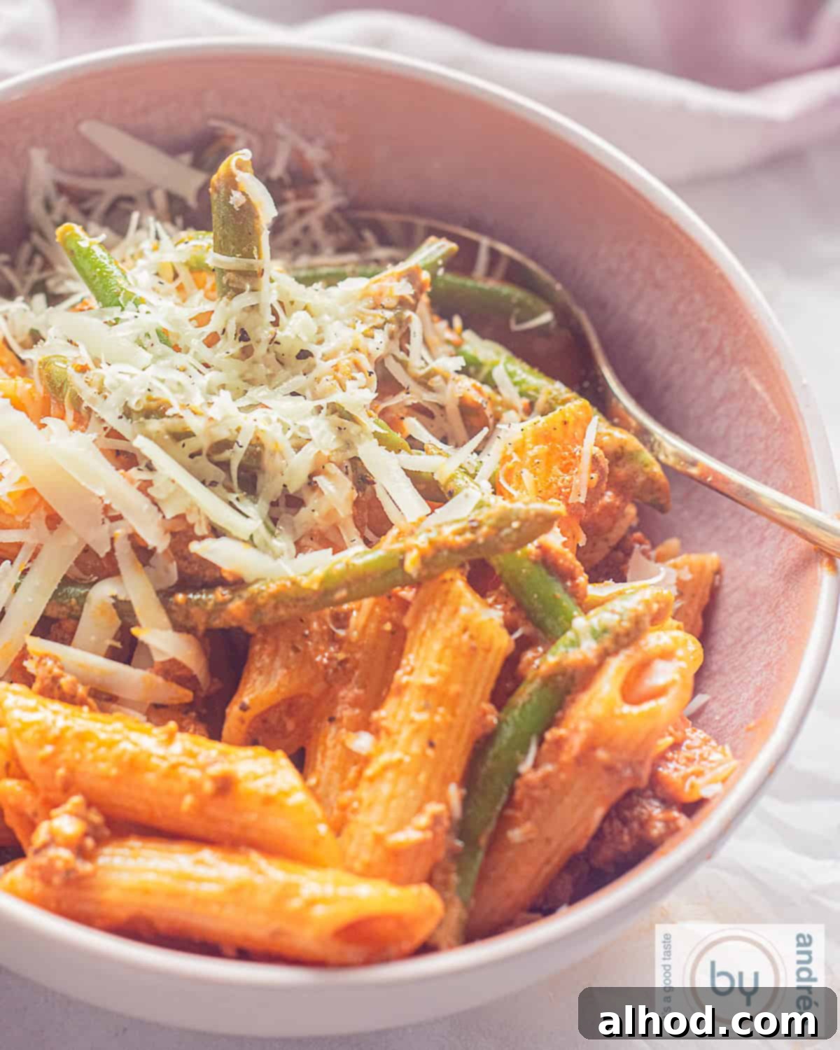 A pink dish to which penne with green beans, minced meat and cheese in a rich tomato sauce has been added.