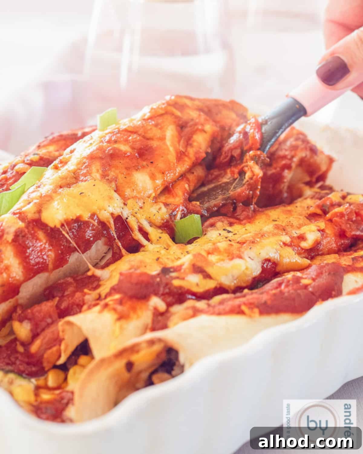 Ultimate Cheesy Beef Enchiladas with a Kick 2 An aerial photo of a white baking dish with ground beef and cheese enchiladas. A spatula scoops one out, highlighting the delicious layers of cheesy ground beef and rich sauce.