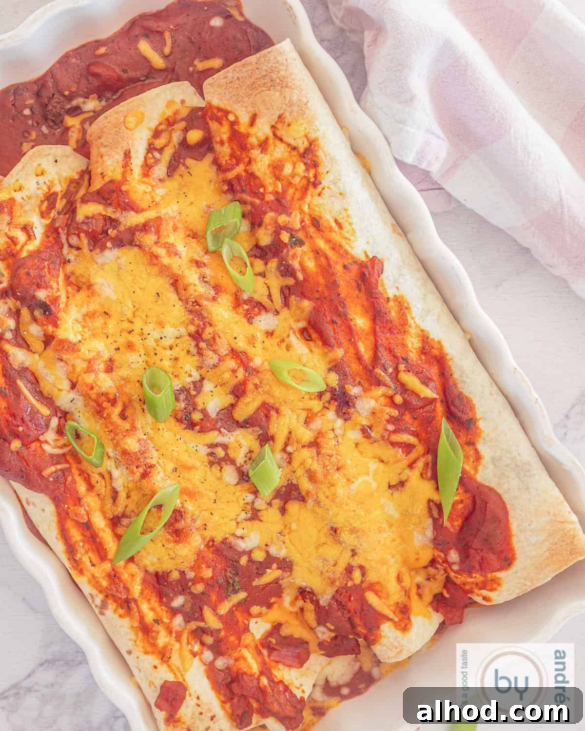 Ultimate Cheesy Beef Enchiladas with a Kick 9 An overhead photo of a white baking dish with four enchiladas side by side, perfectly golden brown and bubbling with melted cheese and rich tomato sauce.