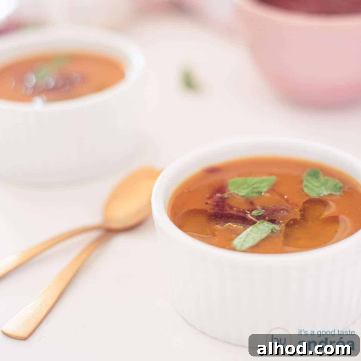 9 Delightfully Light Soups Packed with Fresh Vegetables 2 A square photo with a bowl of spicy pumpkin soup. A second one comes diagonally behind it. Two golden spoons to the left.