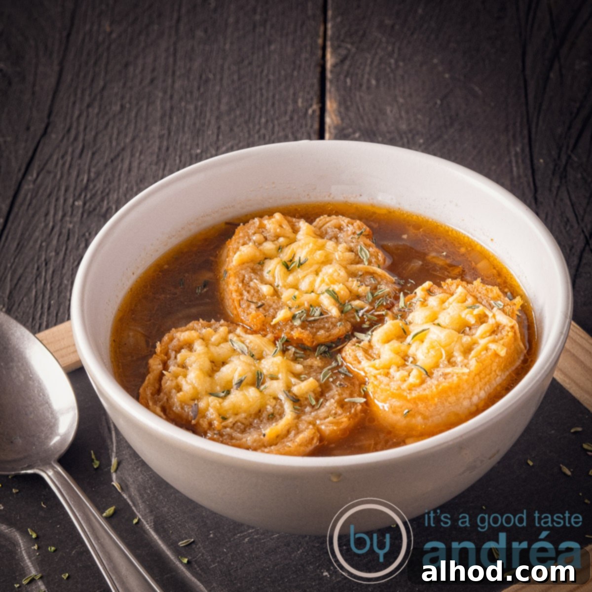 9 Delightfully Light Soups Packed with Fresh Vegetables 4 A square photo with a black background on top of a black plate with a bowl filled with onion soup and baguette au gratin with cheese. A spoon on the left