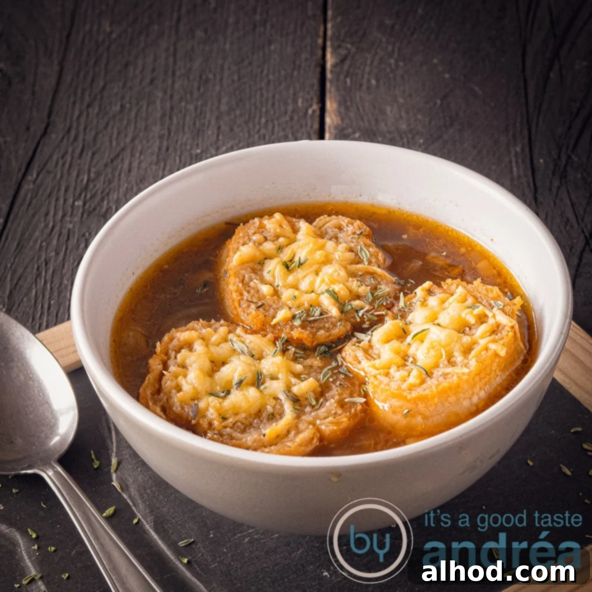 9 Veggie Packed Soups for a Slimmer You 4 A square photo with a black background on top of a black plate with a bowl filled with onion soup and baguette au gratin with cheese. A spoon on the left