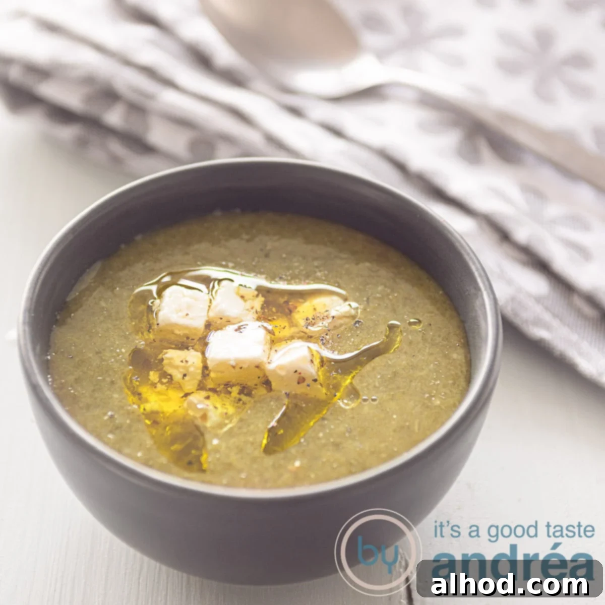 9 Delightfully Light Soups Packed with Fresh Vegetables 7 A square photo with a gray bowl of spinach soup made from fresh spinach, feta and olive oil. A gray white tea towel in the background.