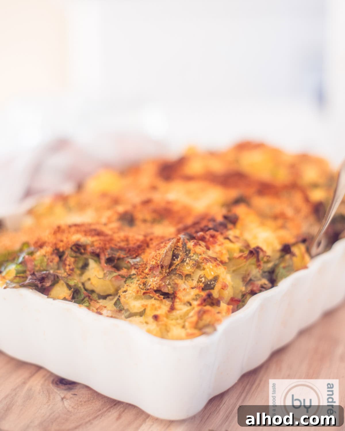Hearty Dutch Endive Bake 3 Part of a white oven dish on a wooden board filled with fried endive stew with minced meat and bacon.