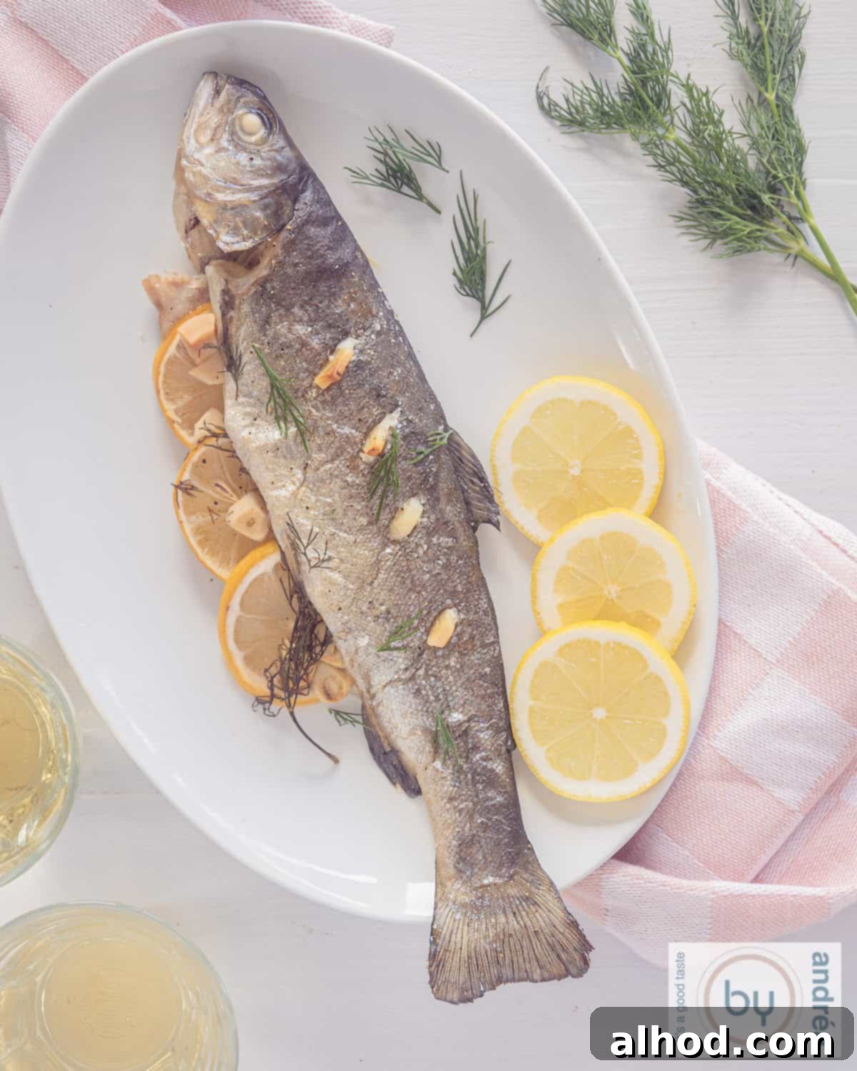 Zesty Lemon Dill Baked Trout 3 A top-down photo of a white plate featuring a perfectly cooked salmon trout, baked in the oven, artfully garnished with fresh lemon wedges, fragrant dill sprigs, and golden brown garlic slices.