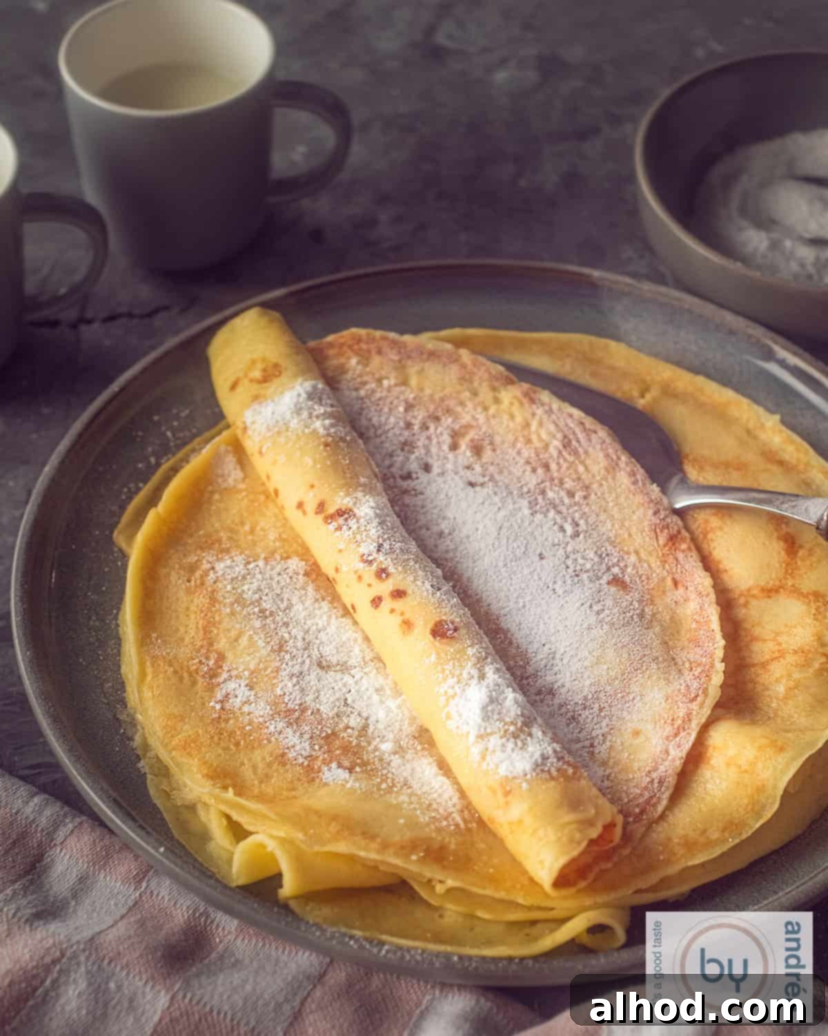 An aerial photo of a stack of pancakes with powdered sugar on a gray background.