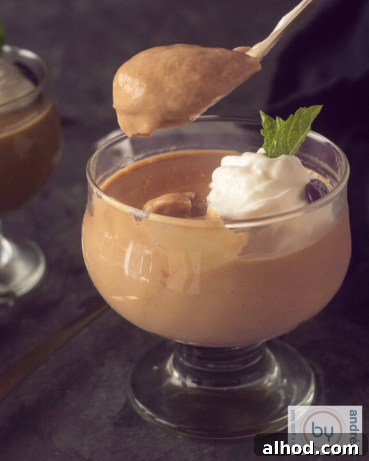 The Ultimate Homemade Dutch Coffee Custard Delight 3 A height photo of a glass filled with hopjesvla and a dollop of whipped cream. A spoon takes a bite out of it.