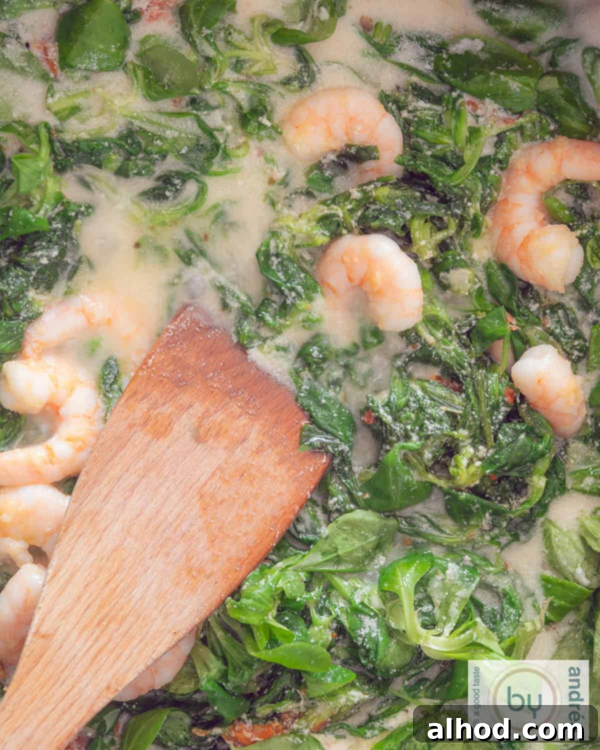 Green lamb's lettuce in cream sauce and shrimp with a wooden spoon.