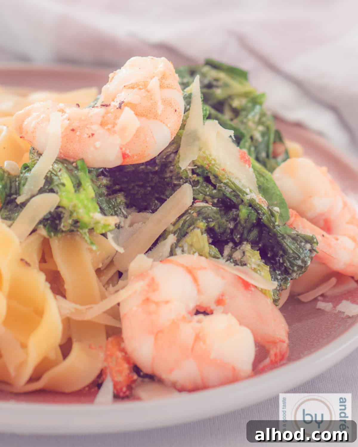 A height photo of tagliatelle, shrimps and lamb's lettuce in a creamy sauce on a pink plate.