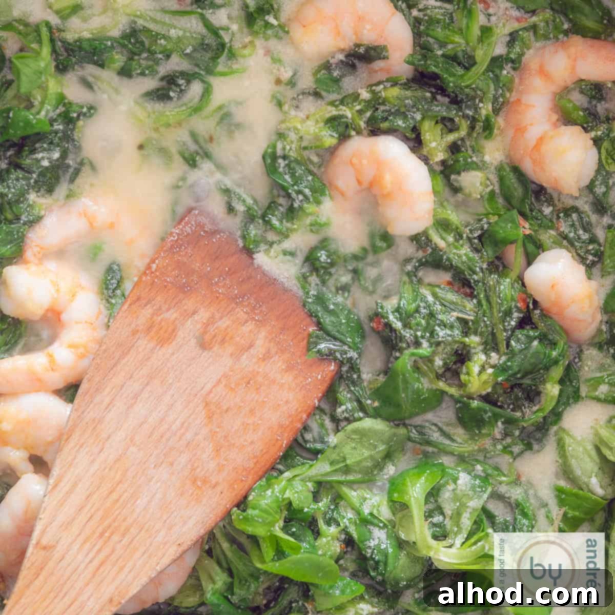 A square photo with lamb's lettuce, creamy sauce, shrimps and a wooden spoon.