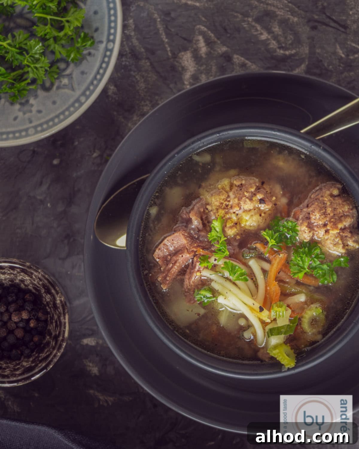 Hearty Dutch Meatball Vegetable Soup 2 A top view of vegetable soup in a dark grey bowl on a grey plate. With meatballs and a parsley garnish