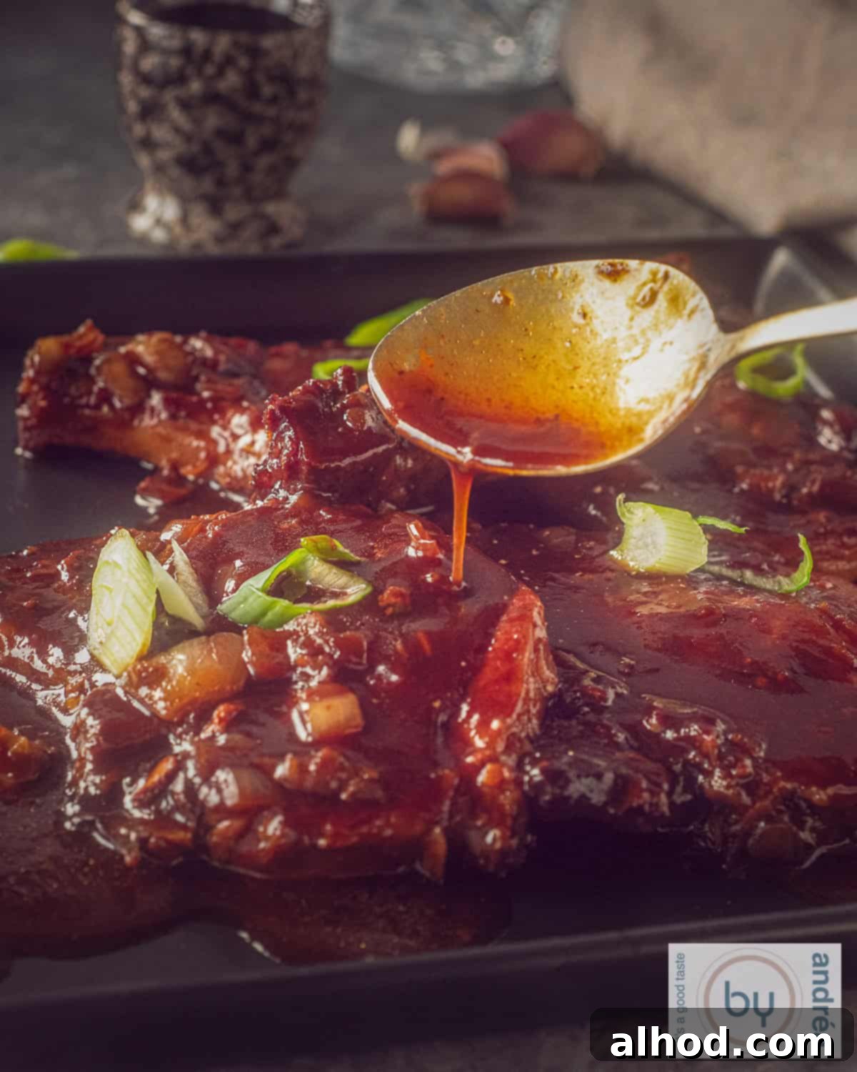 Caramelized Soy Pork Chops 2 A square black plate with chops with sauce. A spoon pours soy sauce on the meat.