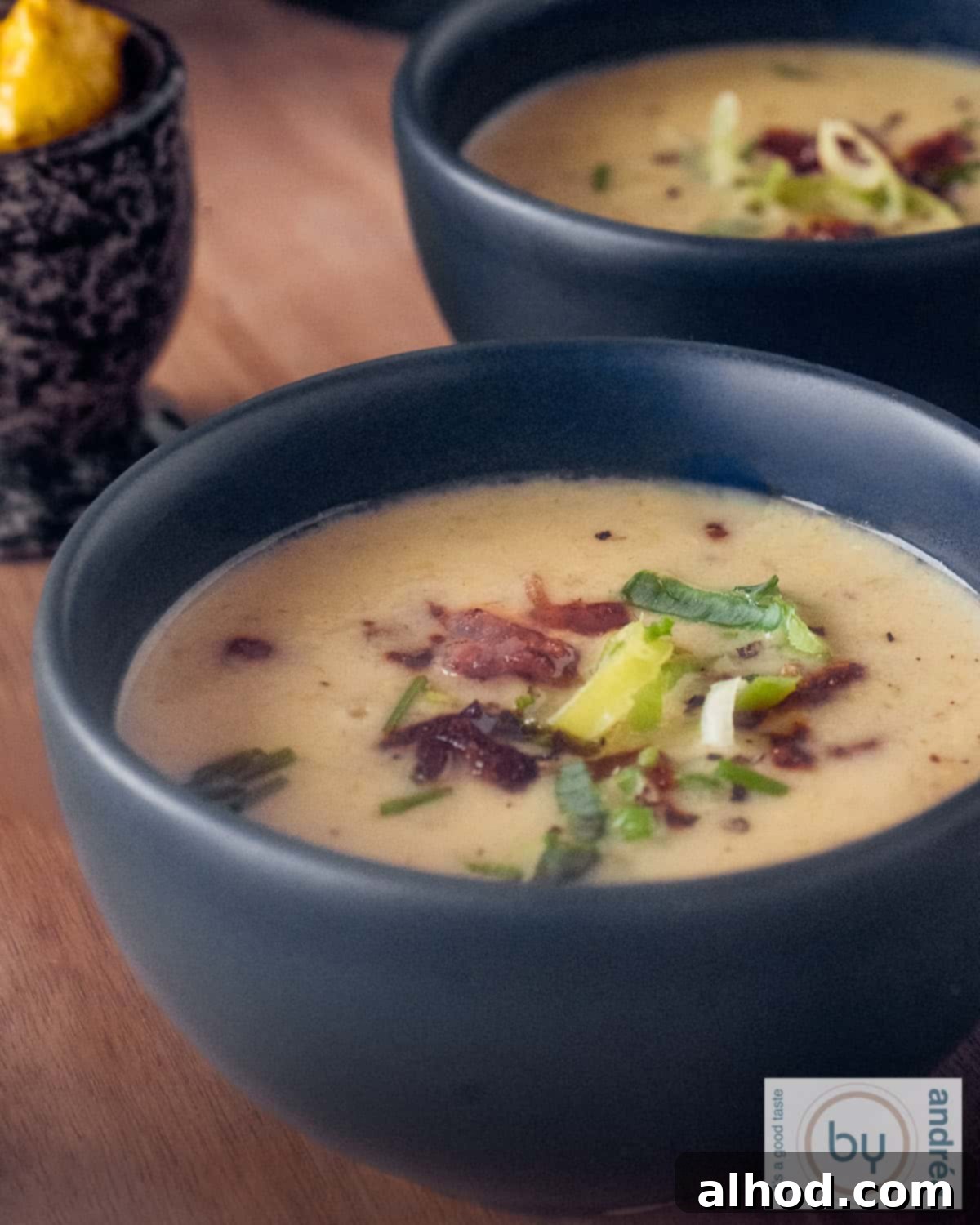Hearty Groninger Mustard Soup with Bacon and Leek 2 Two bowls on a wooden board filled with creamy Dutch Mustard Soup, garnished with crispy bacon and fresh leek.
