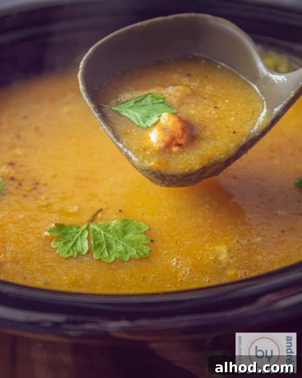 Cozy Creamy Slow Cooker Meatball and Vegetable Soup 2 A photo of a slow cooker with vegetable soup with meatballs and cream. A soup spoon scoops out soup.
