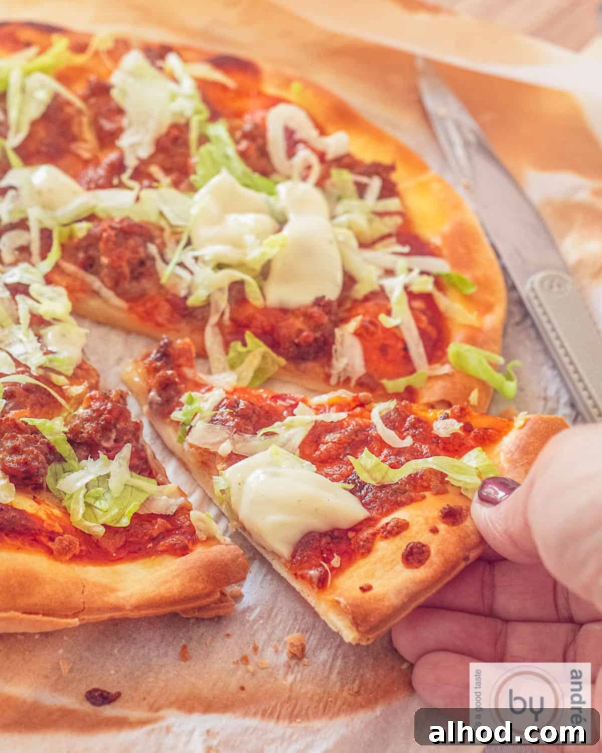 Lightning Fast Beef Taco Pizza with Zesty Garlic Drizzle 2 A pizza taco with iceberg lettuce and garlic sauce. A hand grabs a slice.