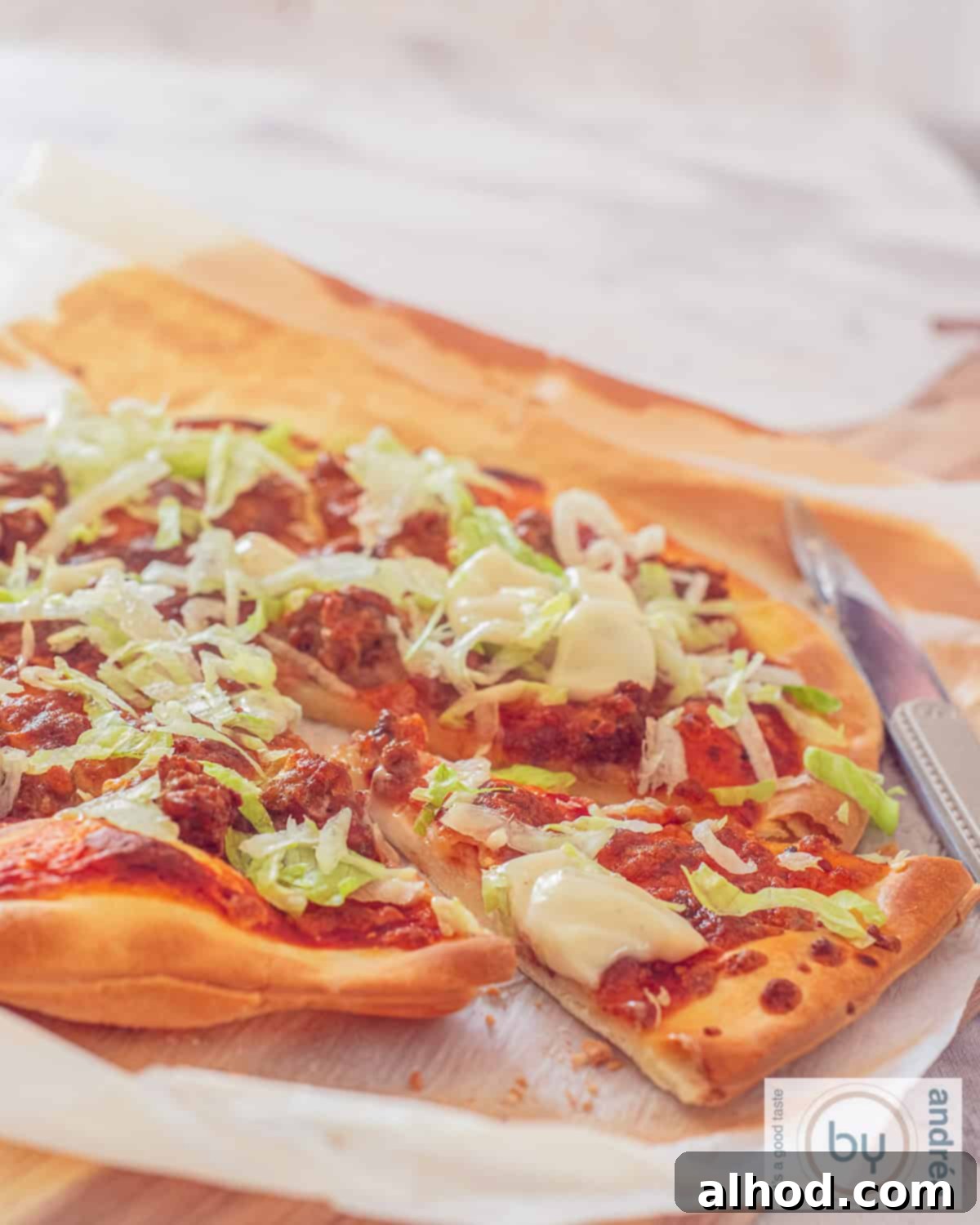 Lightning Fast Beef Taco Pizza with Zesty Garlic Drizzle 3 A pizza with a slice cut out with taco meat, iceberg lettuce and garlic sauce on a wooden board.