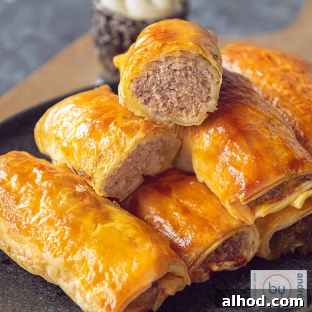 Flaky Dutch Sausage Rolls 4 A square photo of a gray bowl with a stack of puff pastry sausage rolls. One roll cut in half