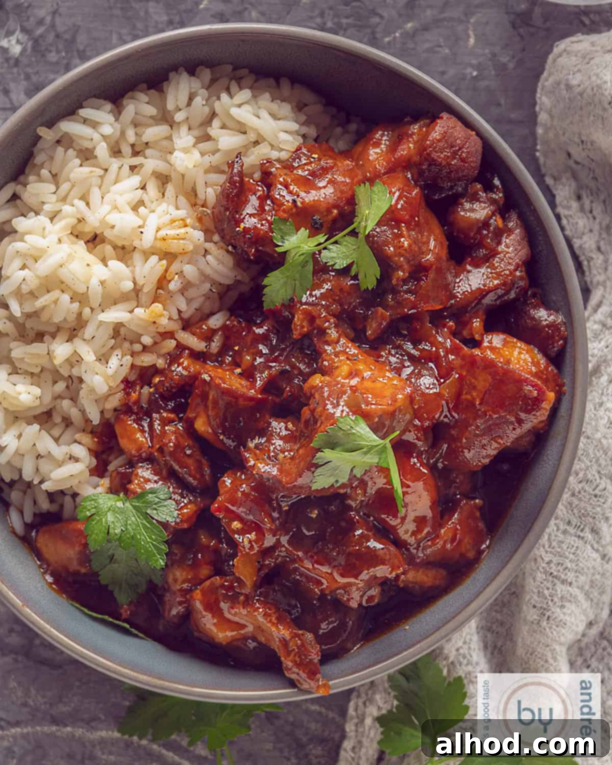 Slow Cooker Indonesian Ajam Pangang 2 A photo from above of a gray bowl filled with slow cooker ajam pangang chicken and fluffy white rice, garnished with fresh herbs.