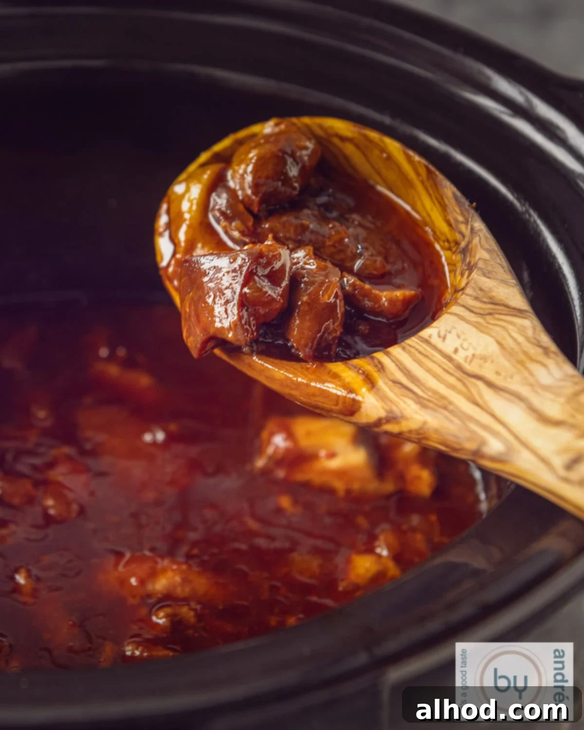 Slow Cooker Indonesian Ajam Pangang 3 A slow cooker with a wooden spoon holding chicken cubes, showing the ajam pangang simmering in the slow cooker.