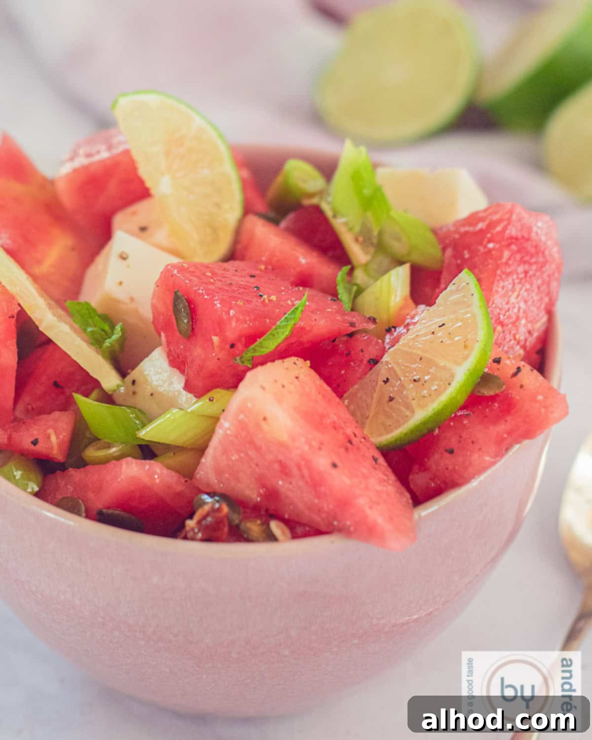Vibrant Watermelon Mint Chevre Salad 2 A photo of a pink bowl with watermelon, lime, spring onion, nuts and goat cheese, highlighting a refreshing summer salad.