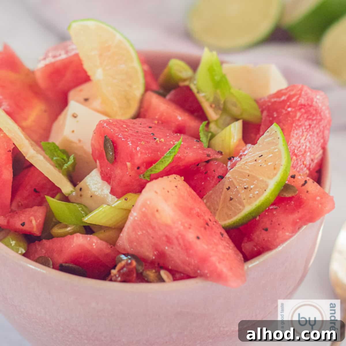 Vibrant Watermelon Mint Chevre Salad 4 A square photo of a melon salad with goat cheese and nuts in a pink bowl, ready to serve.