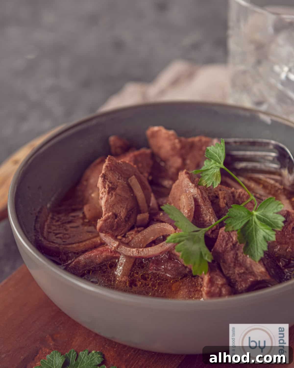 Fall-Apart Slow Cooker Garlic Steak Bites 3 A grey bowl with cubes of entrecote, onion and a delicious sauce. Garnished with parsley.