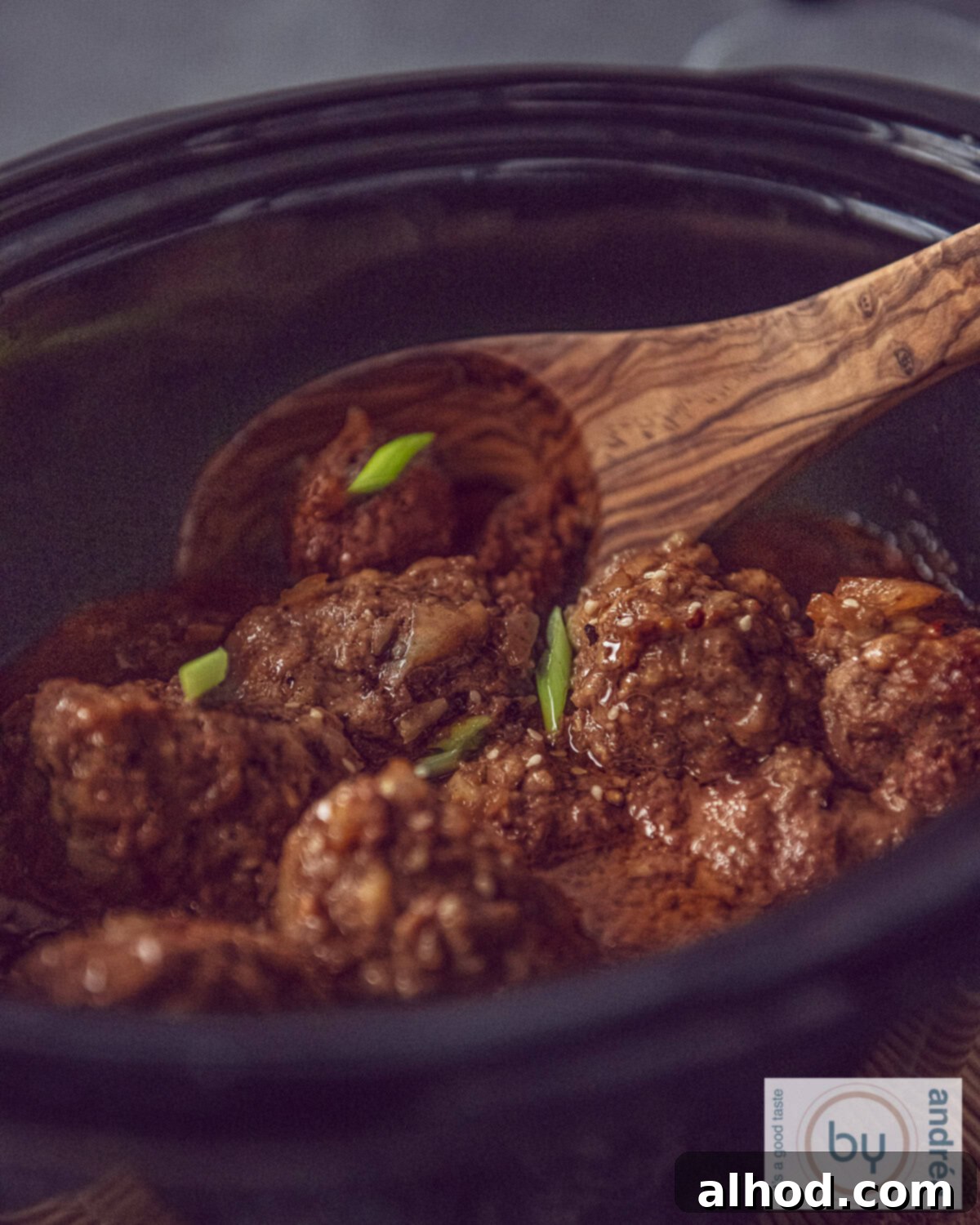 Indonesian Slow Cooker Meatballs in Savory Soy 2 A slow cooker with meatballs in a sweet ketjap sauce and a wooden spoon in it.