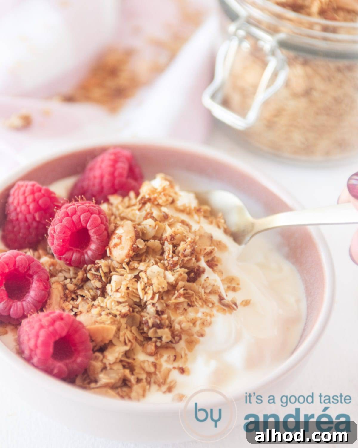 Homemade Almond Coconut Granola Made Simple 4 A vibrant pink bowl showcasing homemade granola with coconut and almonds, artfully topped with fresh raspberries. More granola is visible in the top right corner, ready for serving.