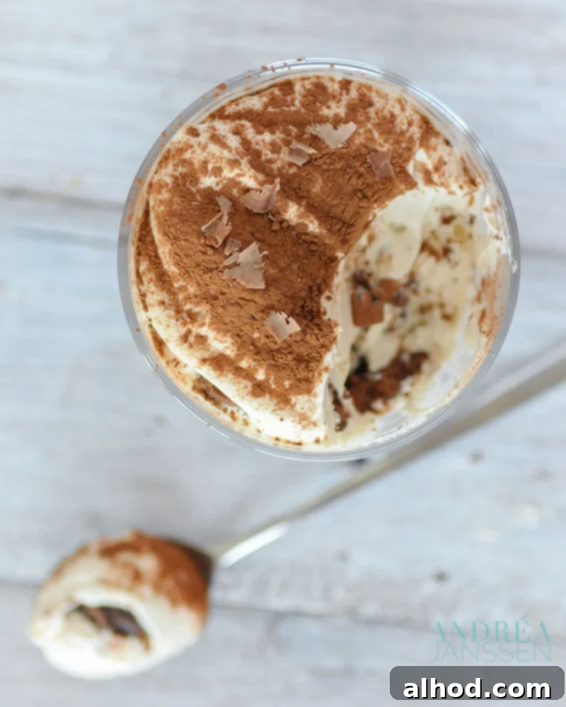A spoon digging into a glass of rich, layered Chocolate Tiramisu, showcasing the creamy mascarpone and chocolate biscuit layers.