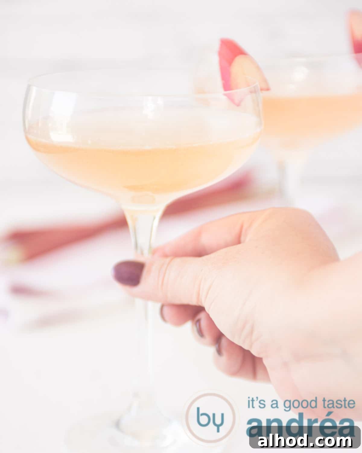 Rhubarb Champagne Sparkler 5 An aerial view with two glasses of champagne rhubarb cocktail with a slice of rhubarb. A hand grabs the front glass.
